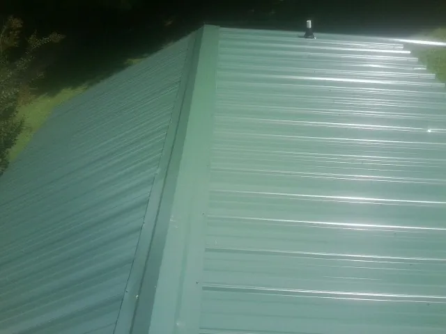New green metal panels meeting at the ridge of a roof — Flat Roof Repair work by our crew in Missouri City